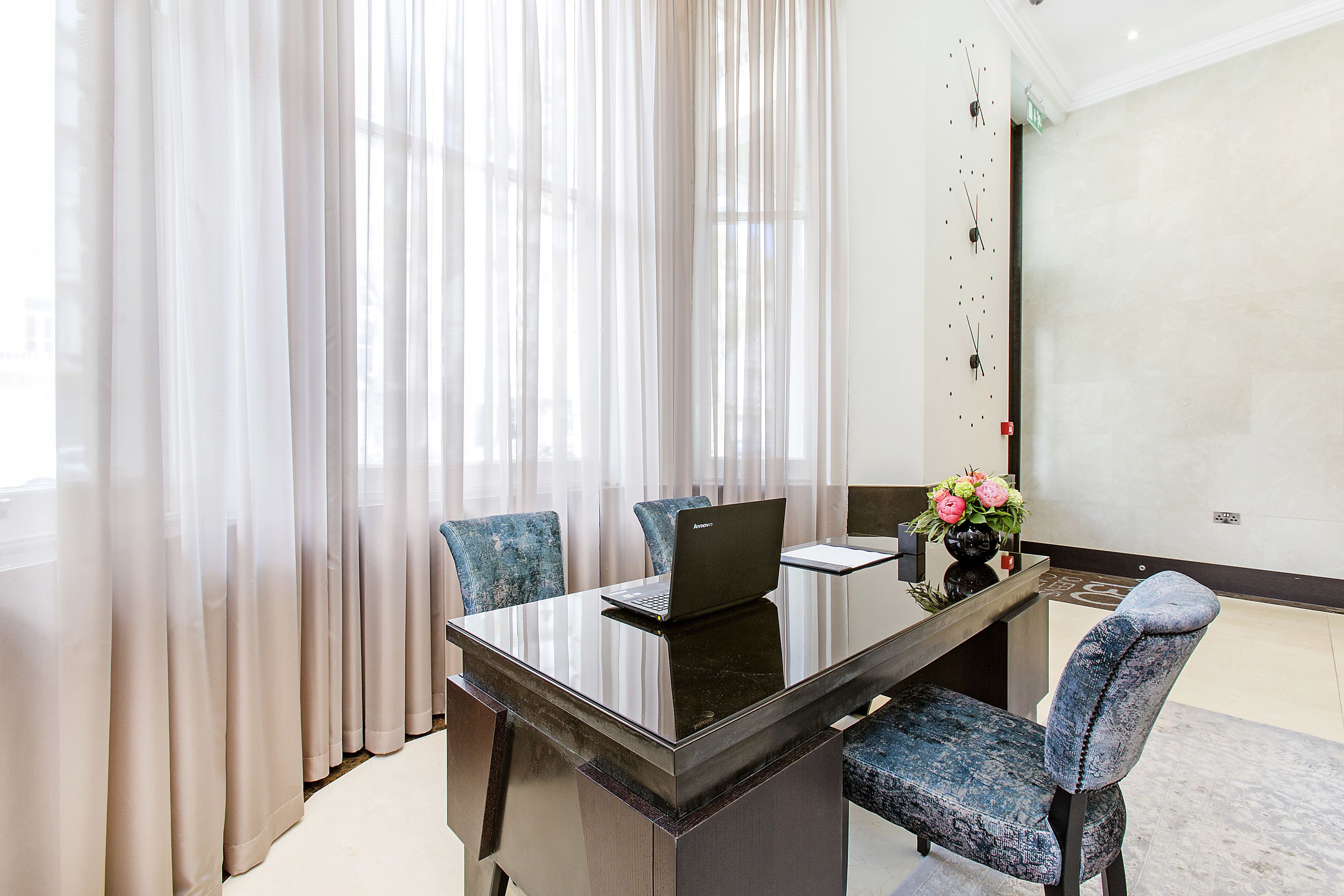 A modern hotel room with a glass table, a laptop, and a vase of flowers.