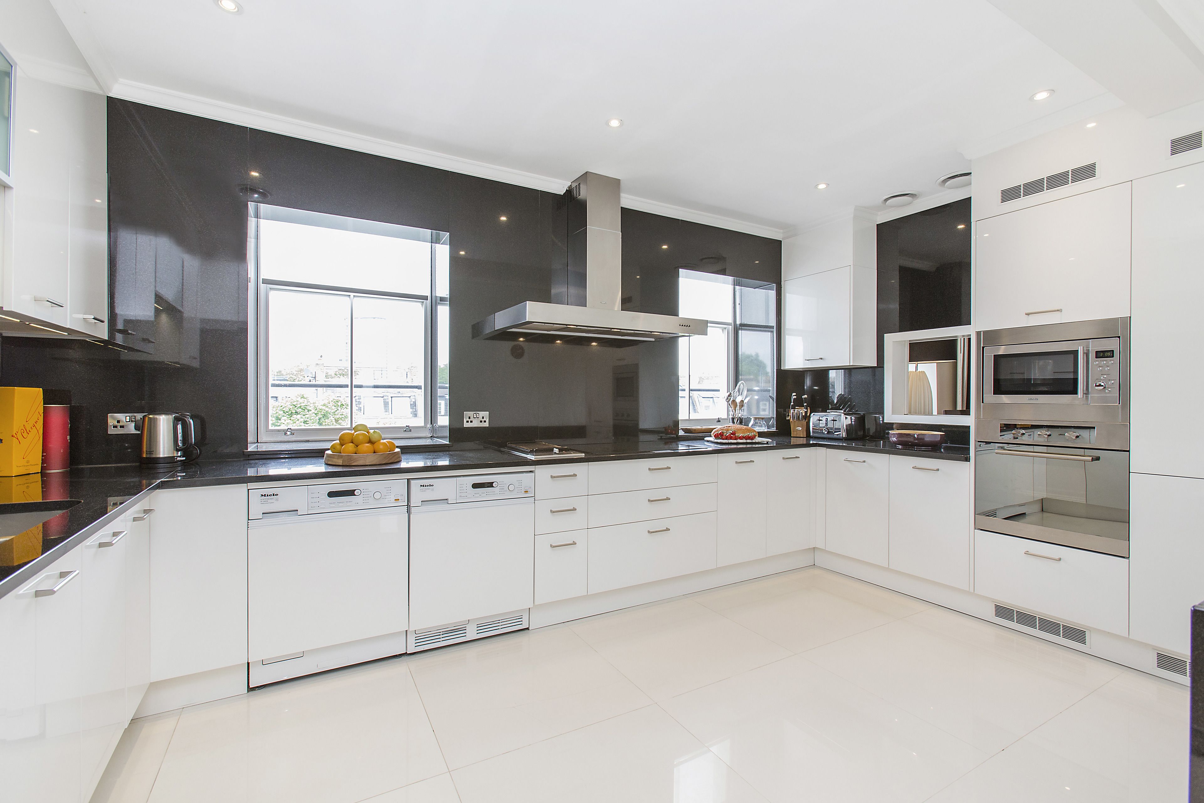 Una cocina moderna con gabinetes blancos, extractor de acero inoxidable y microondas integrado.