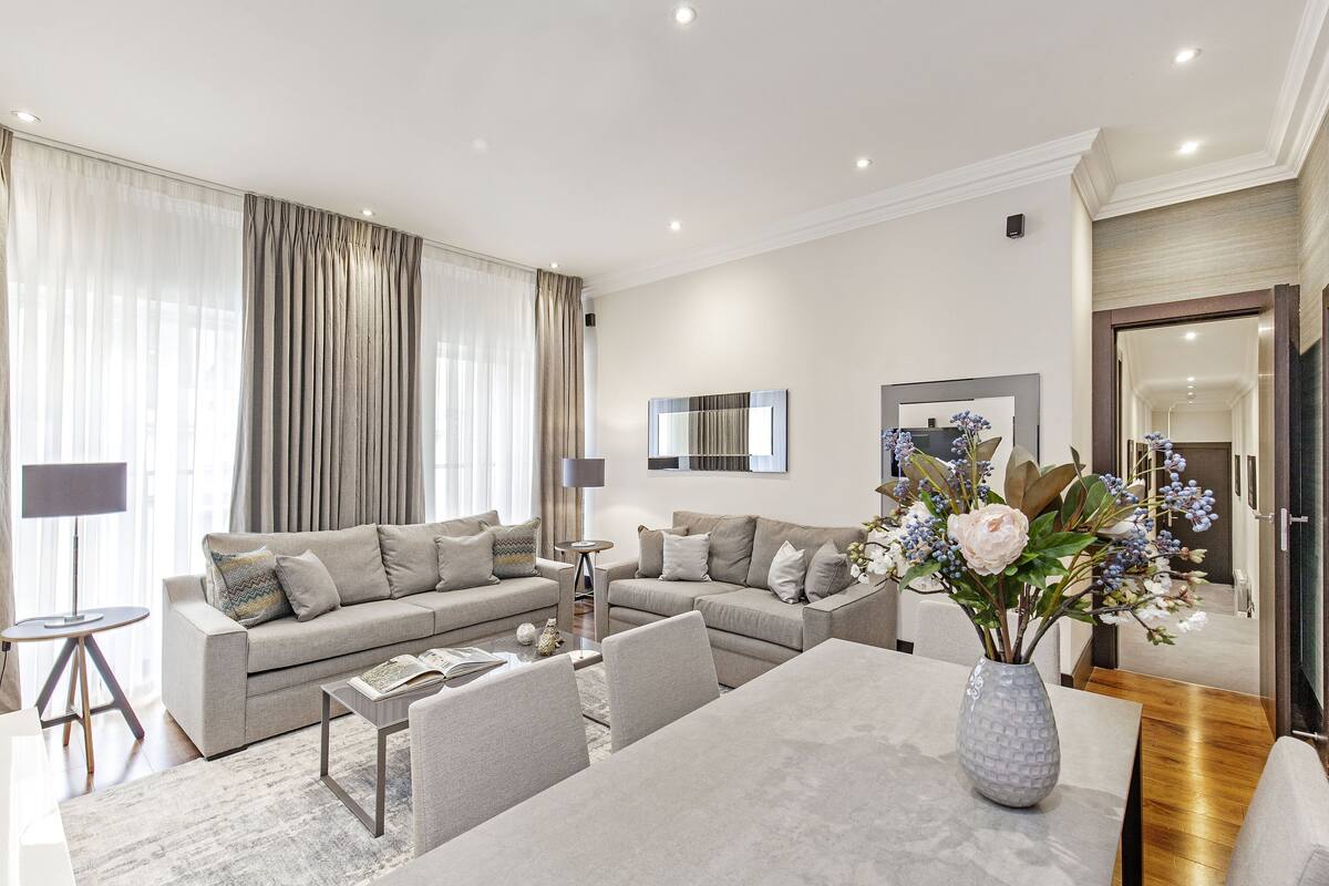 A modern living room with a sofa set, a dining table, and a vase of flowers.