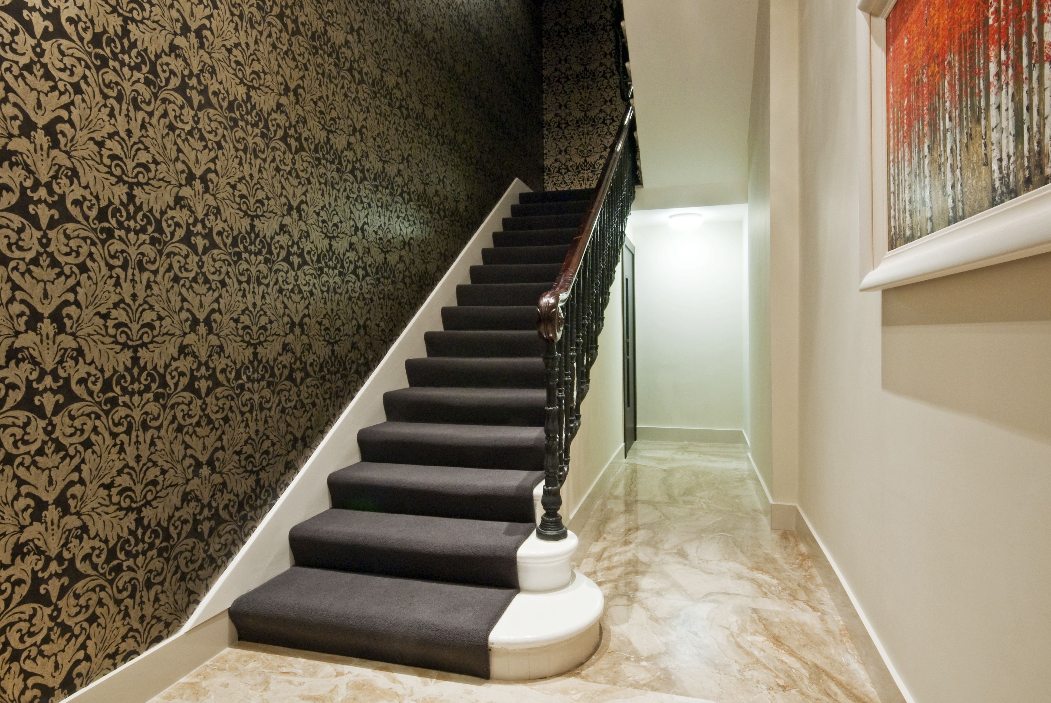 A staircase with dark carpeted steps and a white base, leading to a landing with a black railing.