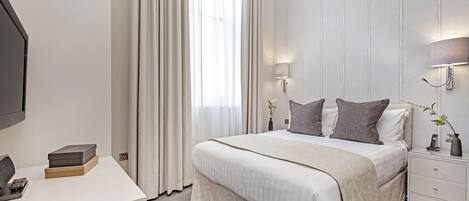 A modern hotel room with a large bed, bedside lamps, a desk with a phone, and a vase with flowers.