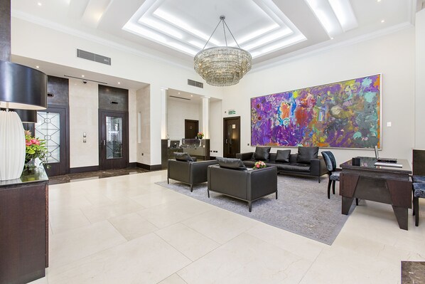 A spacious lobby with a modern chandelier, a large abstract painting, and a reception desk. - 130 Queen's Gate Apartments (London)