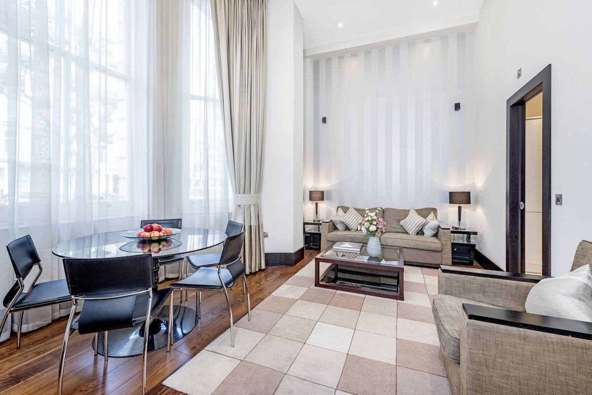 A modern living room with a glass dining table, black chairs, a beige sofa, and a coffee table.