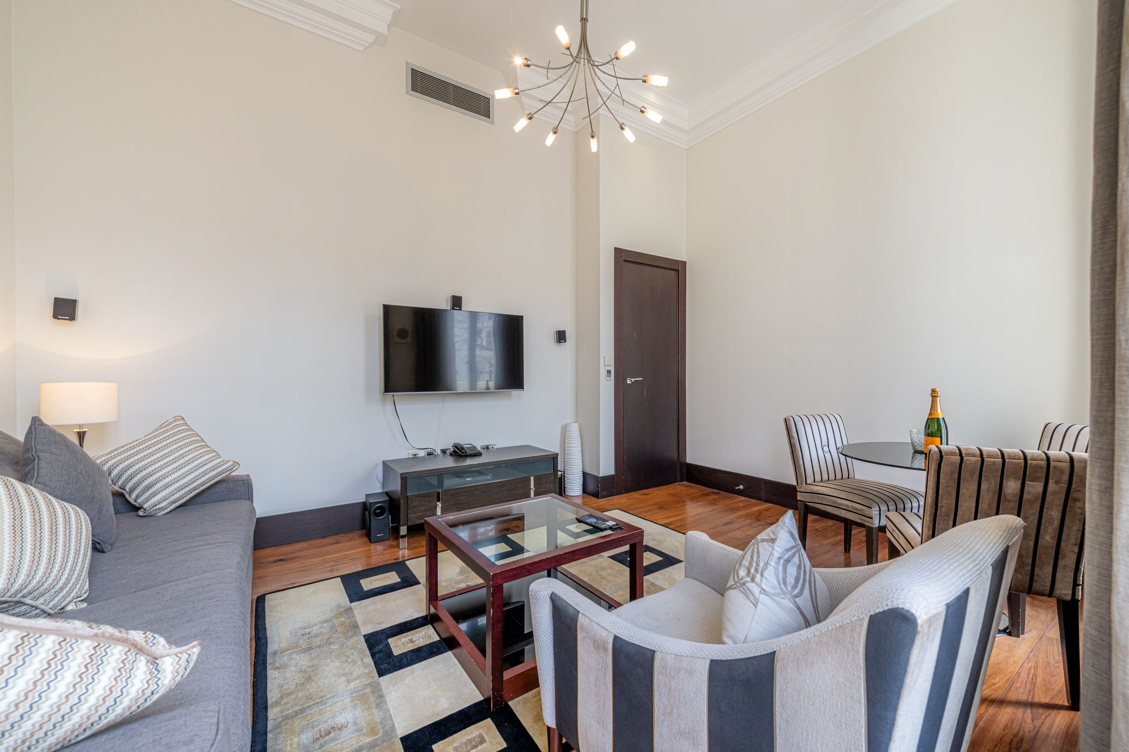A modern living room with a sofa, armchairs, a coffee table, a TV, and a dining area with chairs and a table.