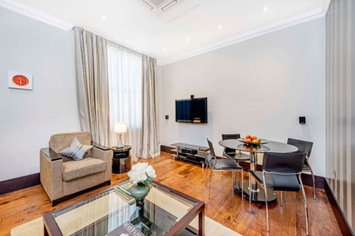Un salon moderne comprenant un canapé, une table basse en verre, une table à manger avec des chaises, un téléviseur à écran plat et une fenêtre avec des rideaux.