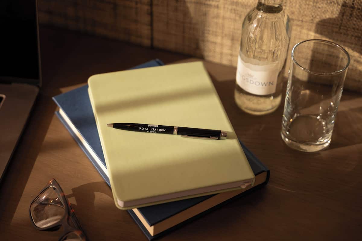 A notebook with a pen on top, a glass of water, and a bottle on a wooden table.