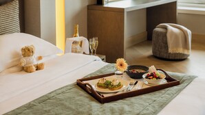 A neatly made bed with a teddy bear, a tray with breakfast, and a view of the room. - Royal Garden Hotel (London)