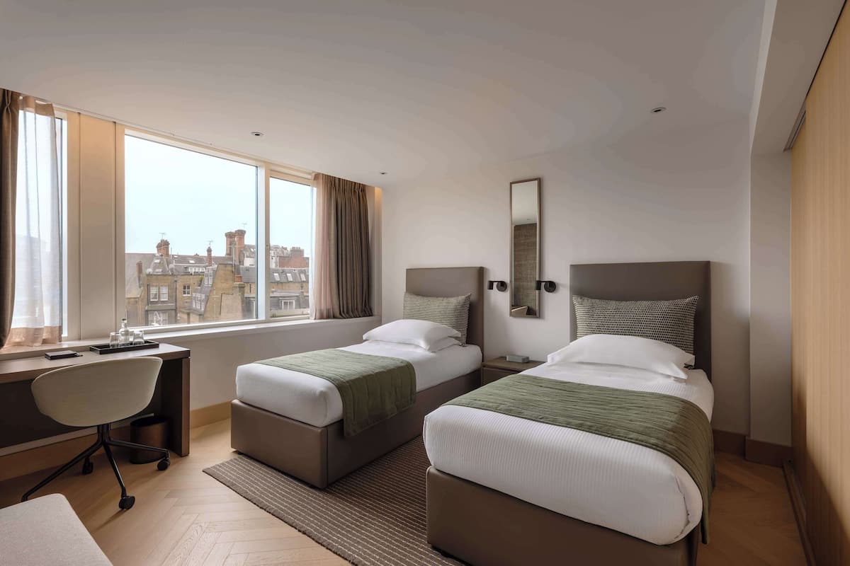 Une chambre d’hôtel avec deux lits, un bureau, une chaise et une grande fenêtre donnant sur la ville.