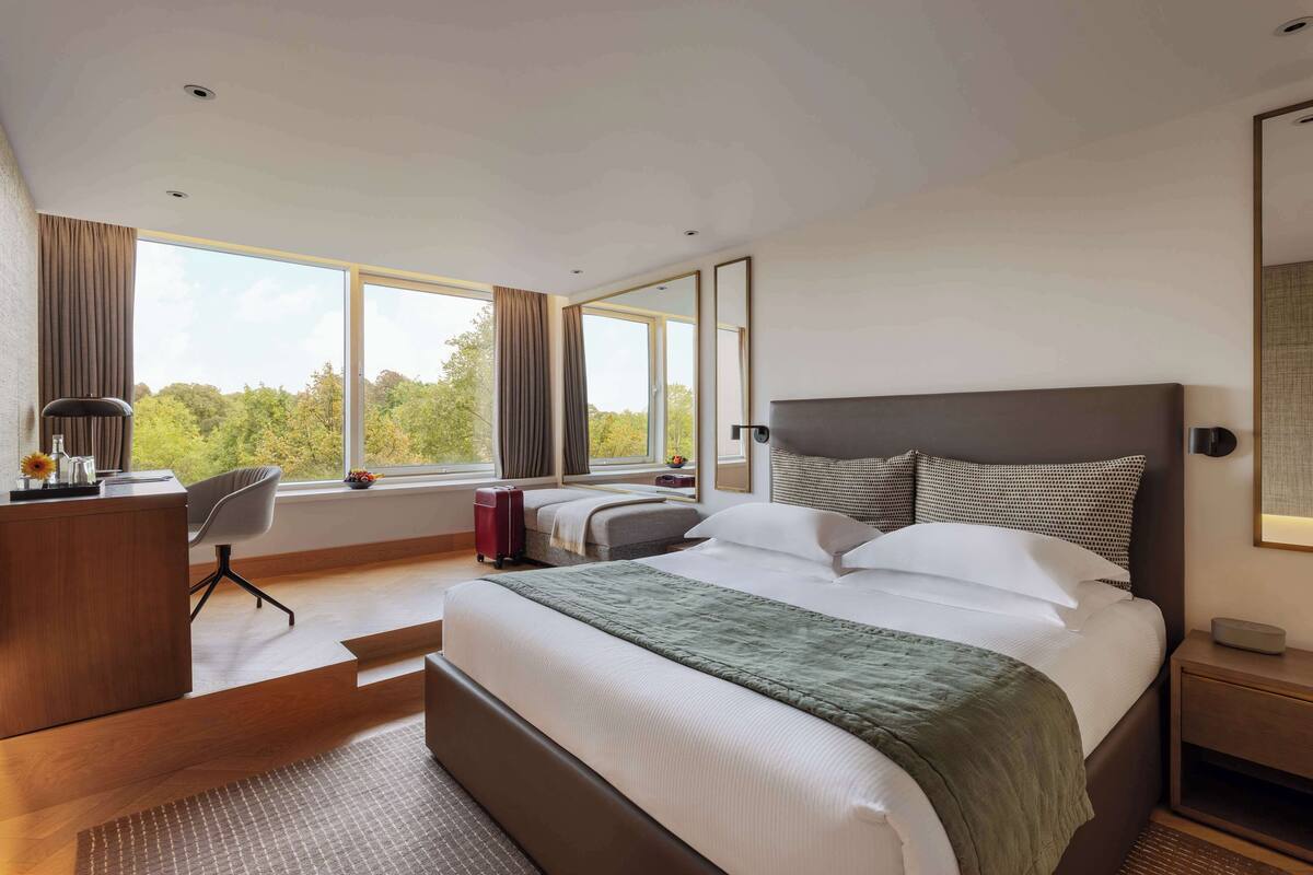 Une chambre d’hôtel moderne, dotée d’un grand lit, d’un bureau, d’une chaise et offrant une vue sur les arbres par la fenêtre.