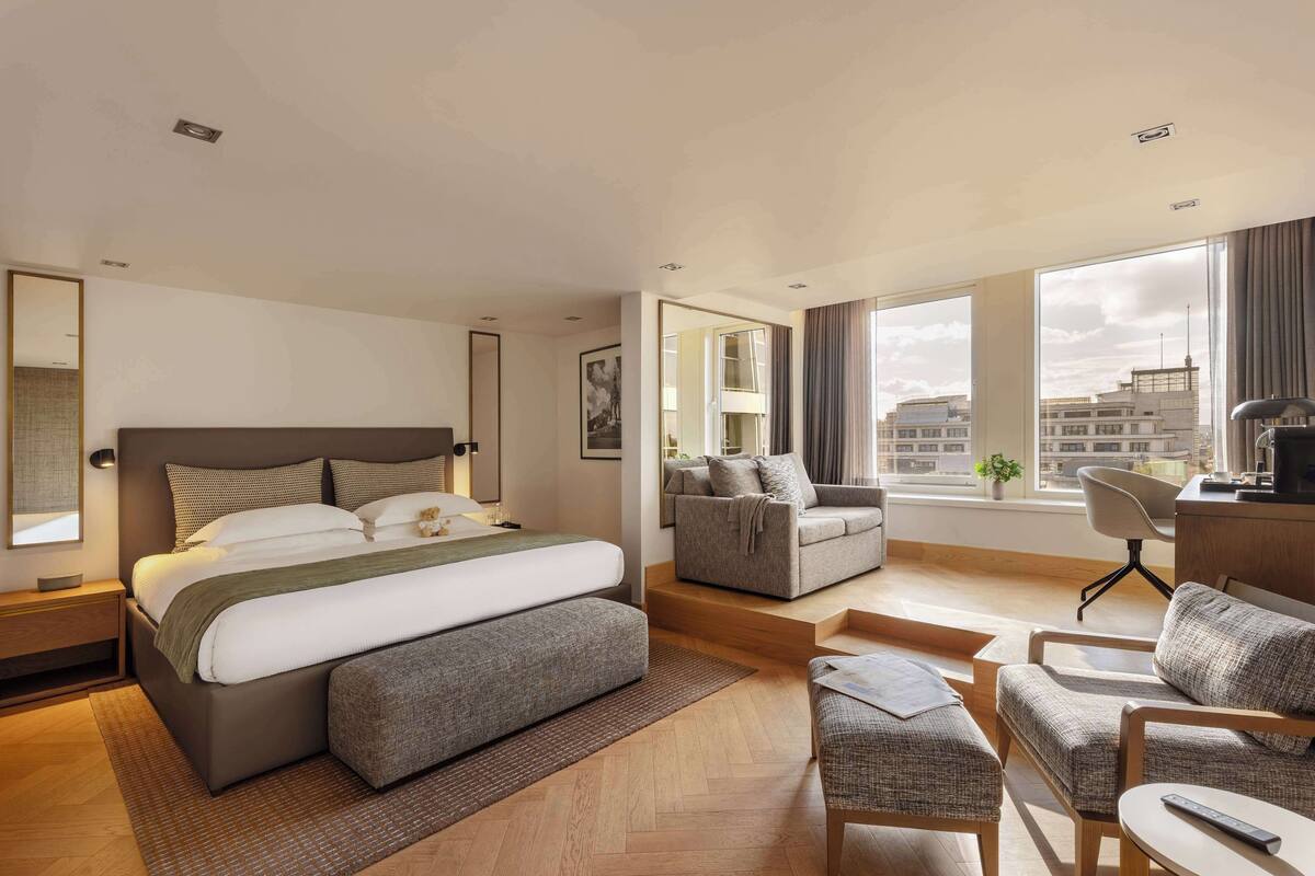 Une chambre d’hôtel moderne, dotée d’un grand lit, d’un canapé, d’un bureau et offrant une vue sur la ville.