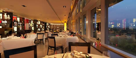 Ein Restaurant mit gedeckten Tischen, Blick auf die Stadt durch große Fenster und Regale mit dekorativen Gegenständen.