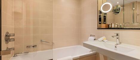 Un baño moderno con ducha de vidrio, una bañera blanca y un espejo grande con luz circular.