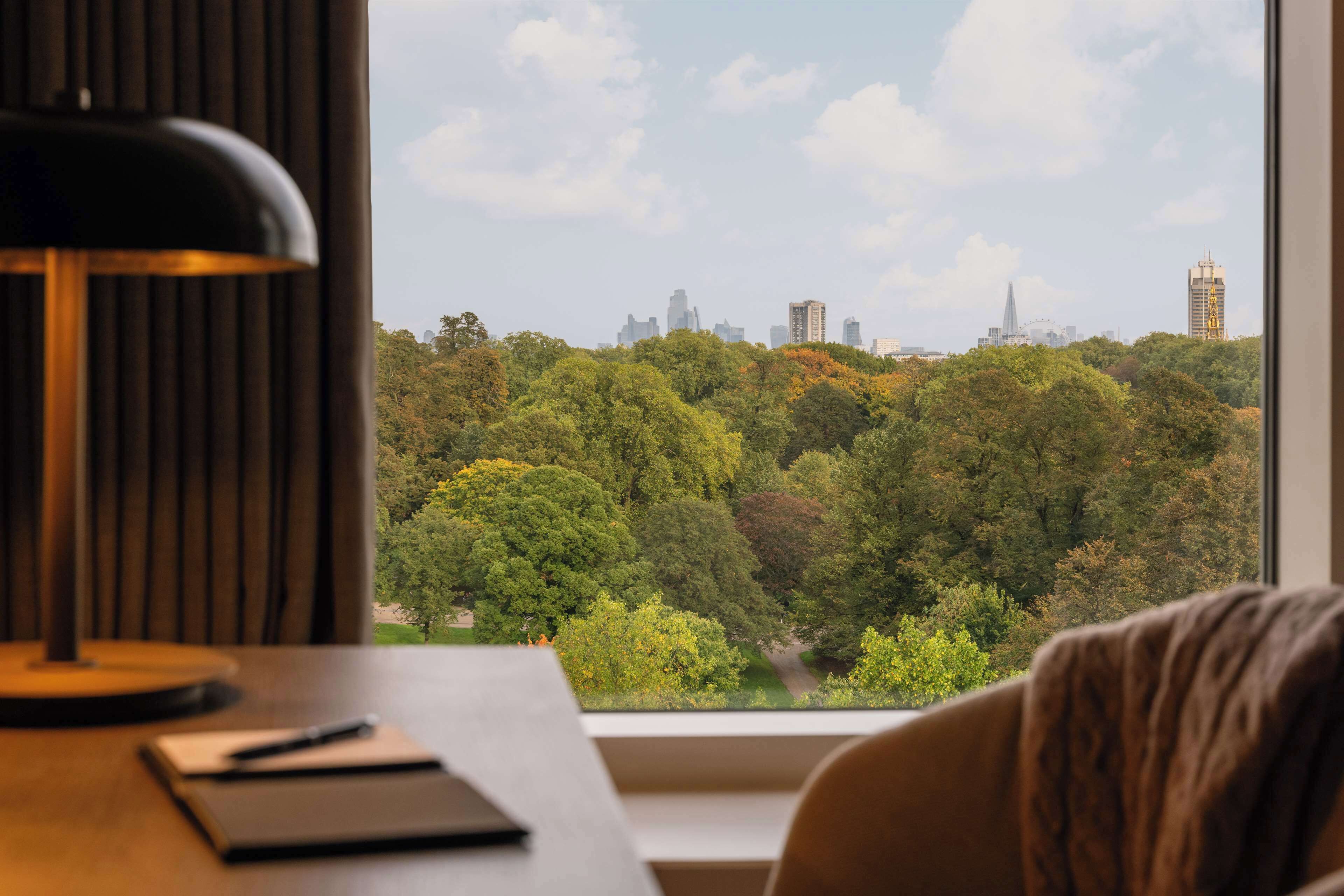 A room with a desk, a lamp, and a view of a city skyline through a window.