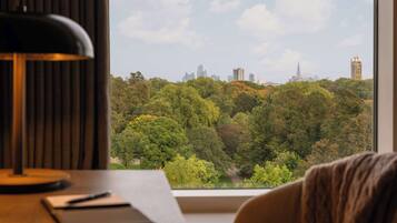 A room with a desk, a lamp, and a view of a city skyline through a window.
