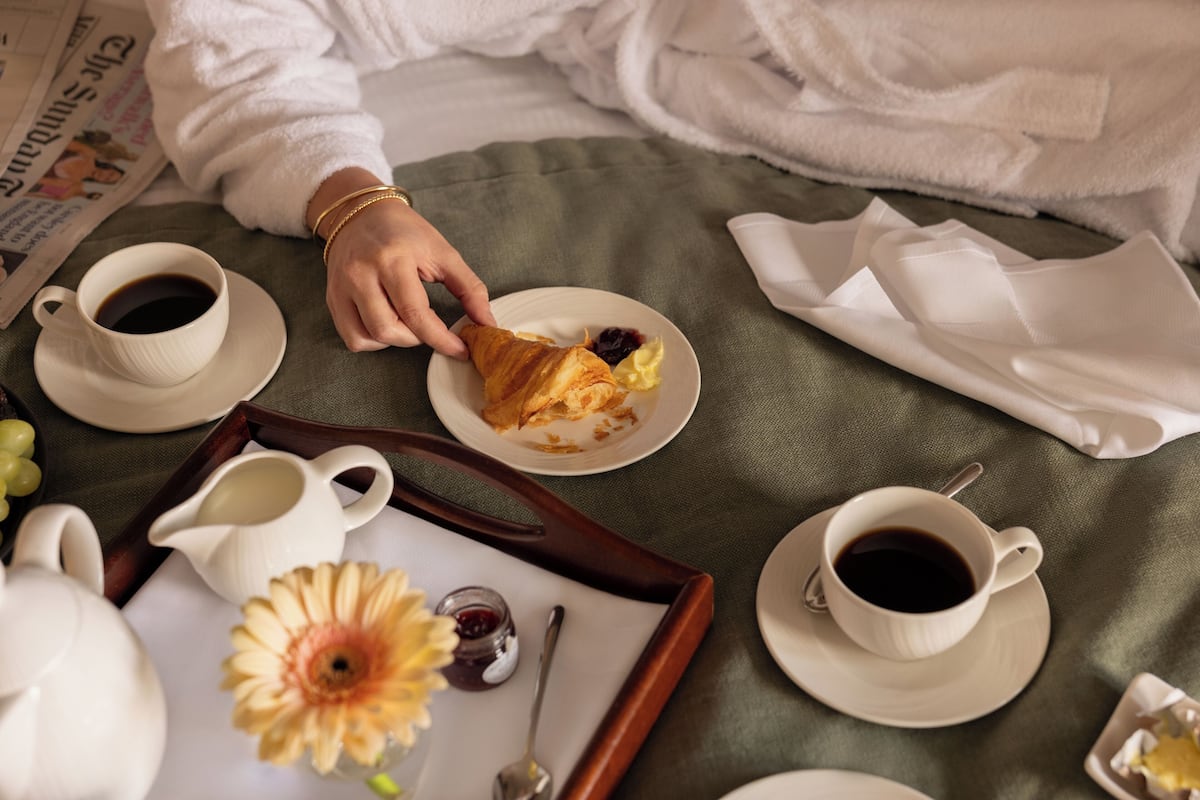 A breakfast setting with a croissant, coffee, and a flower arrangement on a tray.