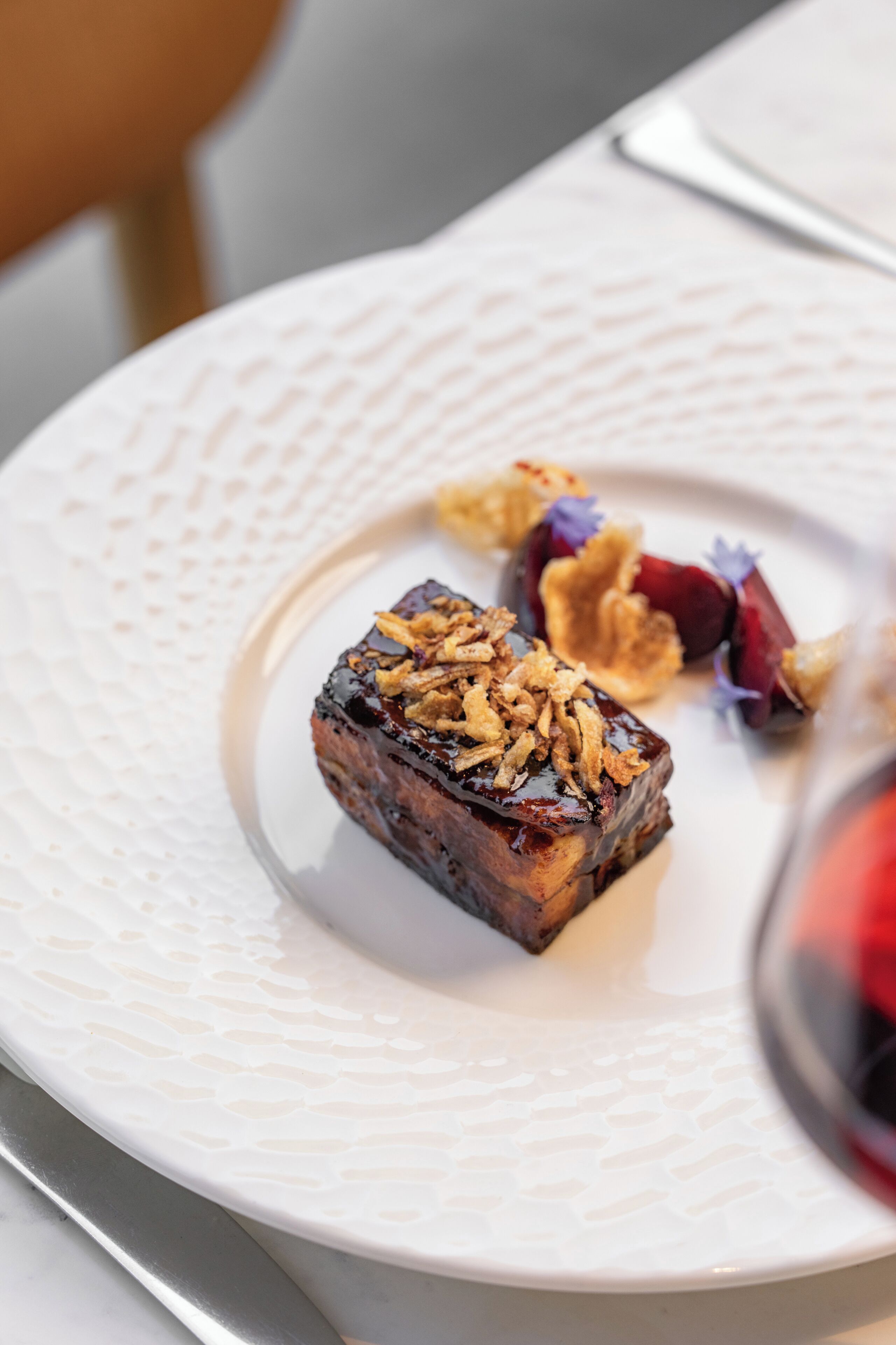 A white plate with a piece of food topped with granola and a small portion of fruit.