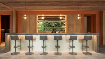 A bar area with a long counter, five stools, and pendant lighting.
