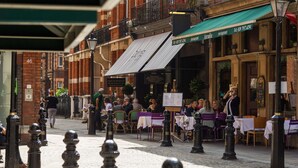 Una calle con terraza para comer al aire libre, un edificio de ladrillo y pilares a lo largo de la acera.