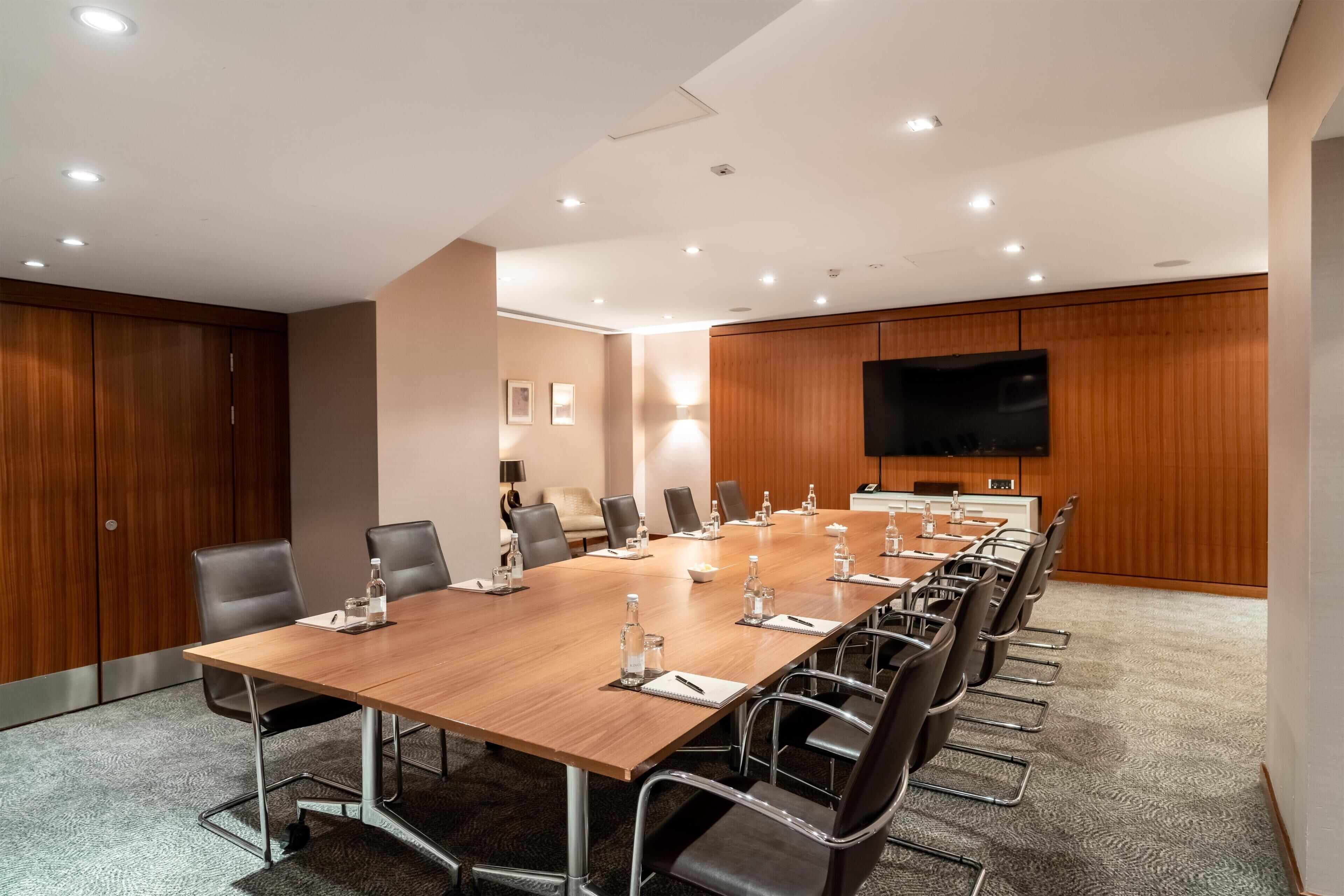 A conference room with a long table, chairs, and a flat-screen TV on the wall.