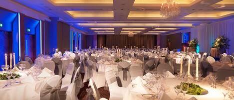 A banquet hall with round tables, white tablecloths, and candle centerpieces.