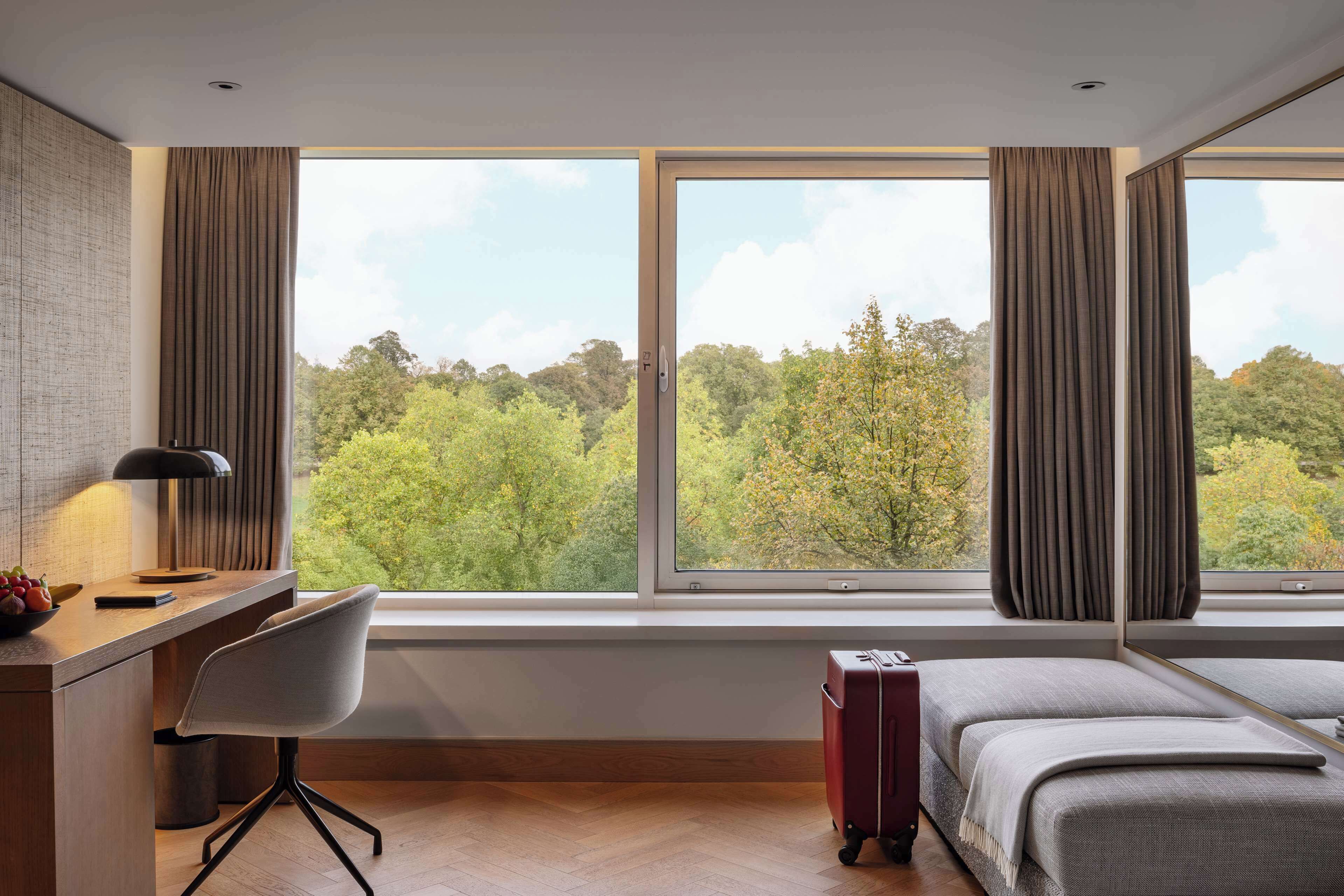 A hotel room with a desk, chair, bed, and a suitcase.