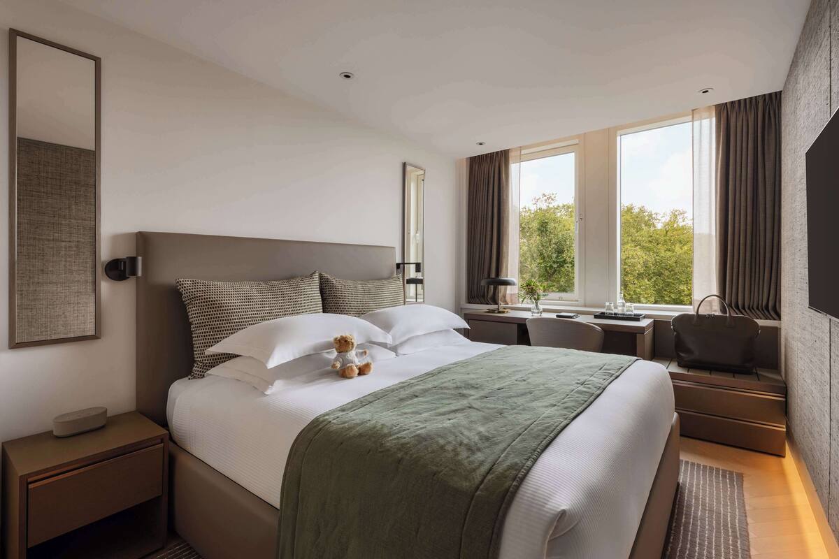 Une chambre d’hôtel moderne avec un grand lit, un bureau, une chaise, une fenêtre avec des rideaux et une table de chevet avec une lampe.