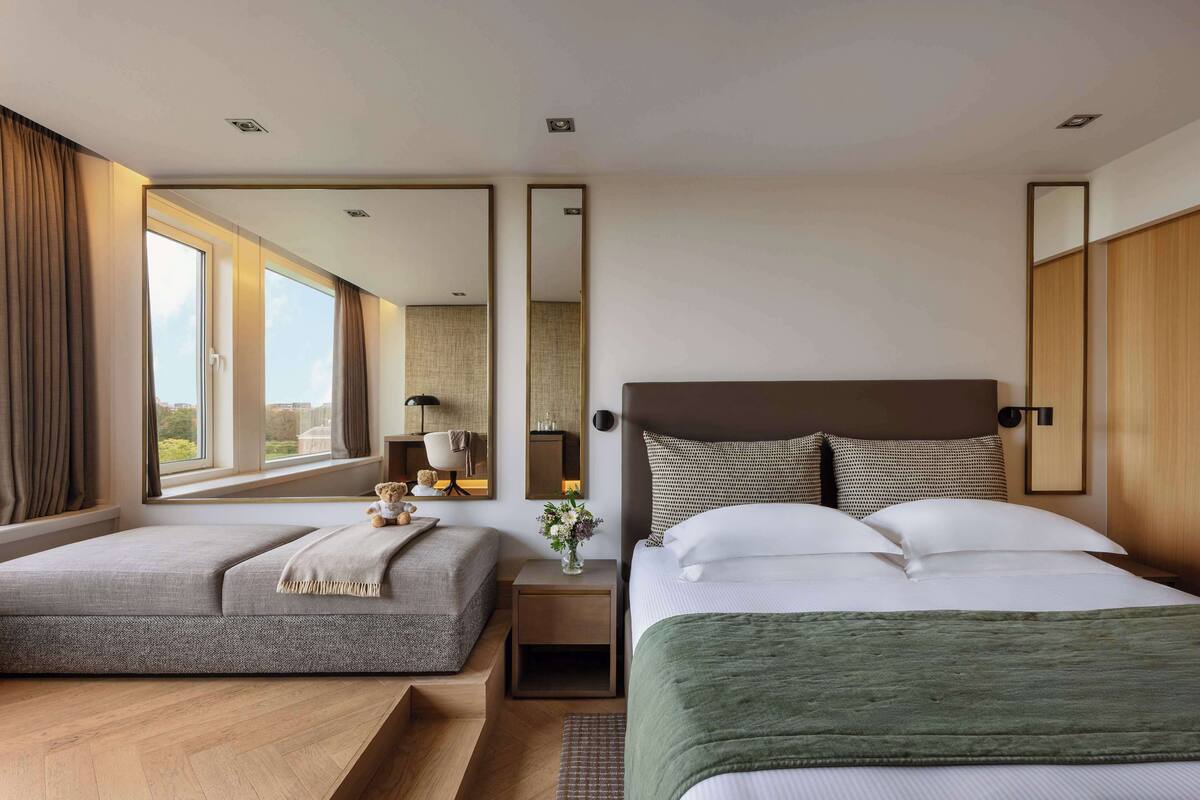 Une chambre d’hôtel avec deux lits, une grande fenêtre, une table de chevet avec une lampe et un miroir.