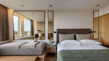 A hotel room with two beds, a large window, a nightstand with a lamp, and a mirror.