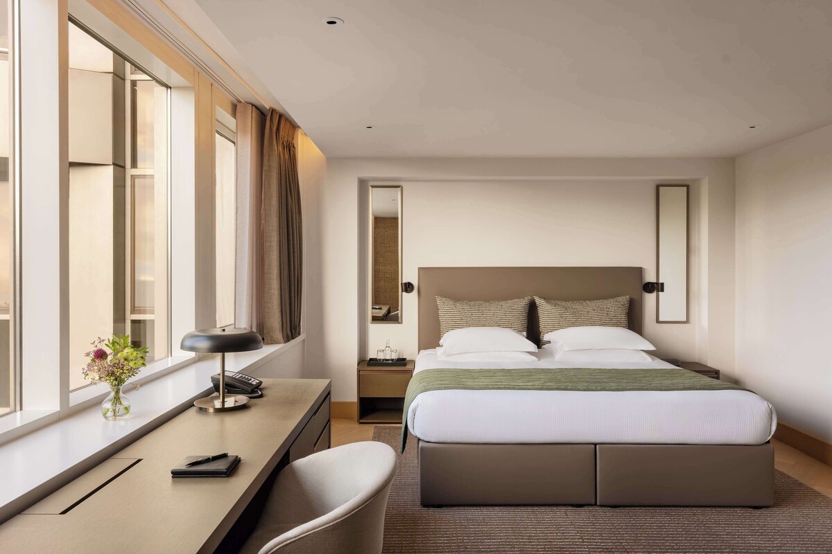 A hotel room with a bed, desk, chair, and a window with curtains.