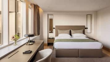 A hotel room with a bed, desk, chair, and a window with curtains.