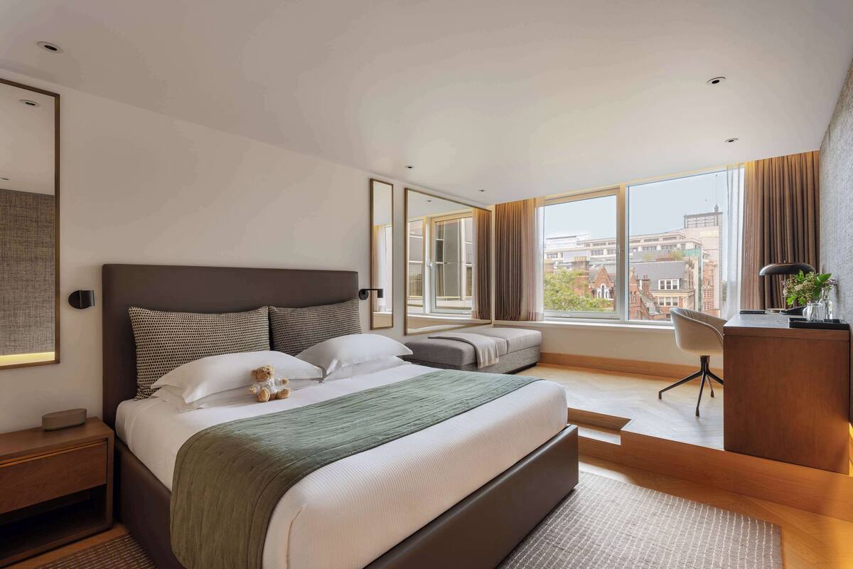 Une chambre d’hôtel moderne, dotée d’un grand lit, d’un bureau et offrant une vue sur les bâtiments grâce à de grandes fenêtres.