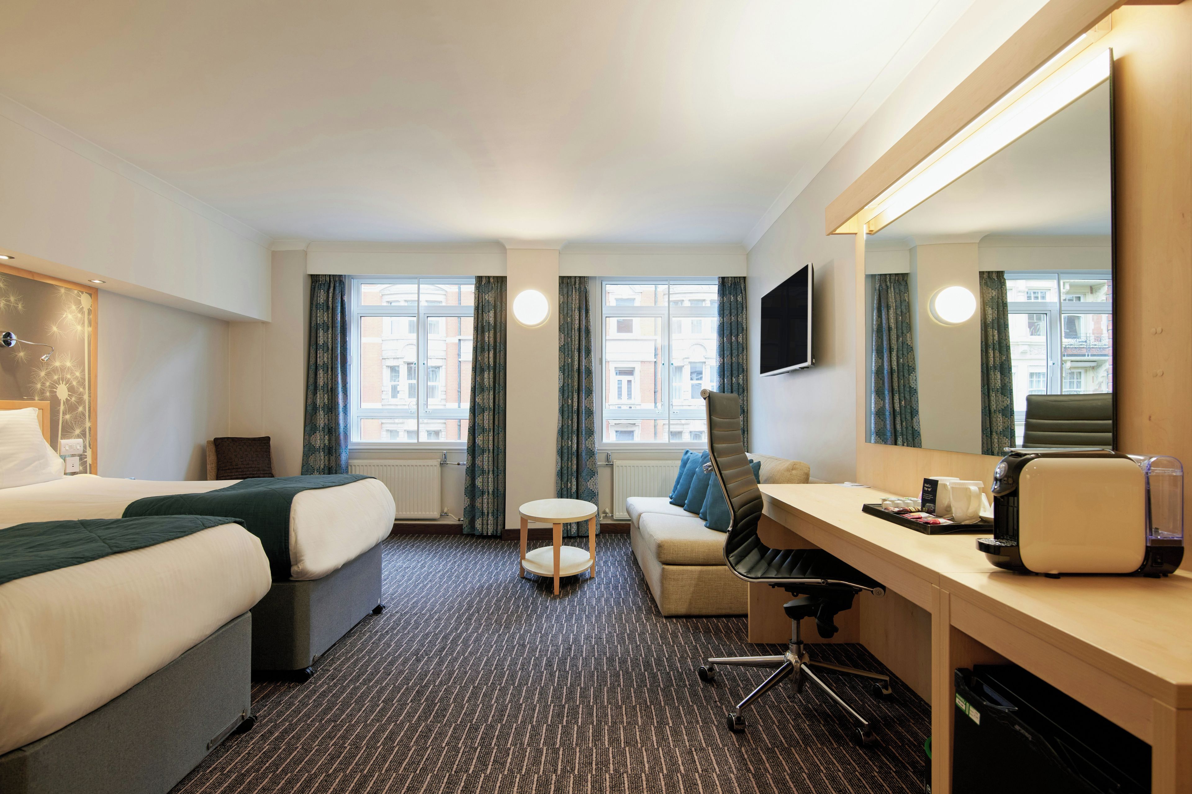 Ett hotellrum med en säng, ett skrivbord, en stol, en soffa och en stor spegel.