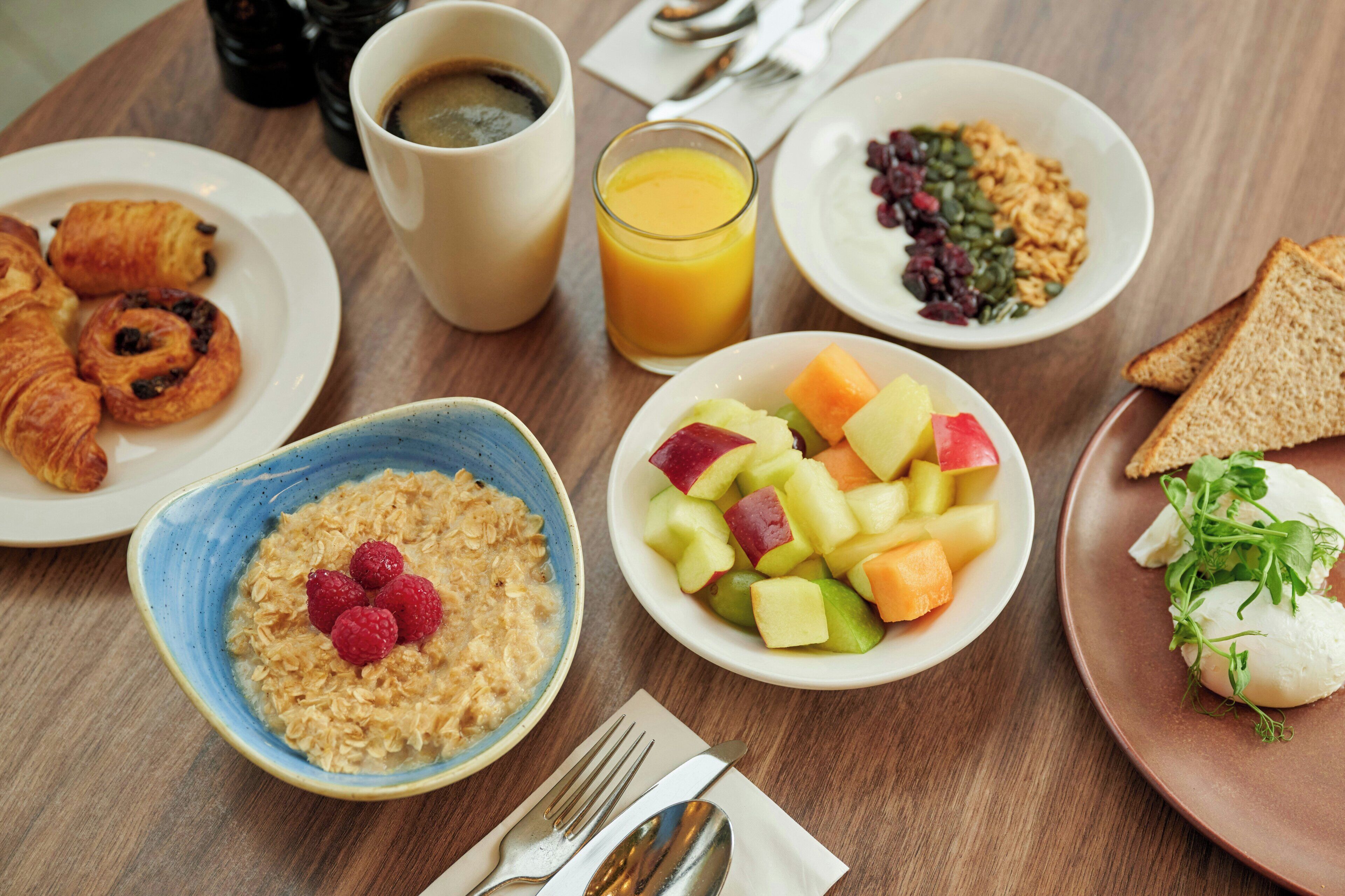 A breakfast table with croissants, cereal, fruit, toast, and a coffee cup.