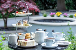 A three-tiered tea service set outdoors with a fountain and flowers in the background.