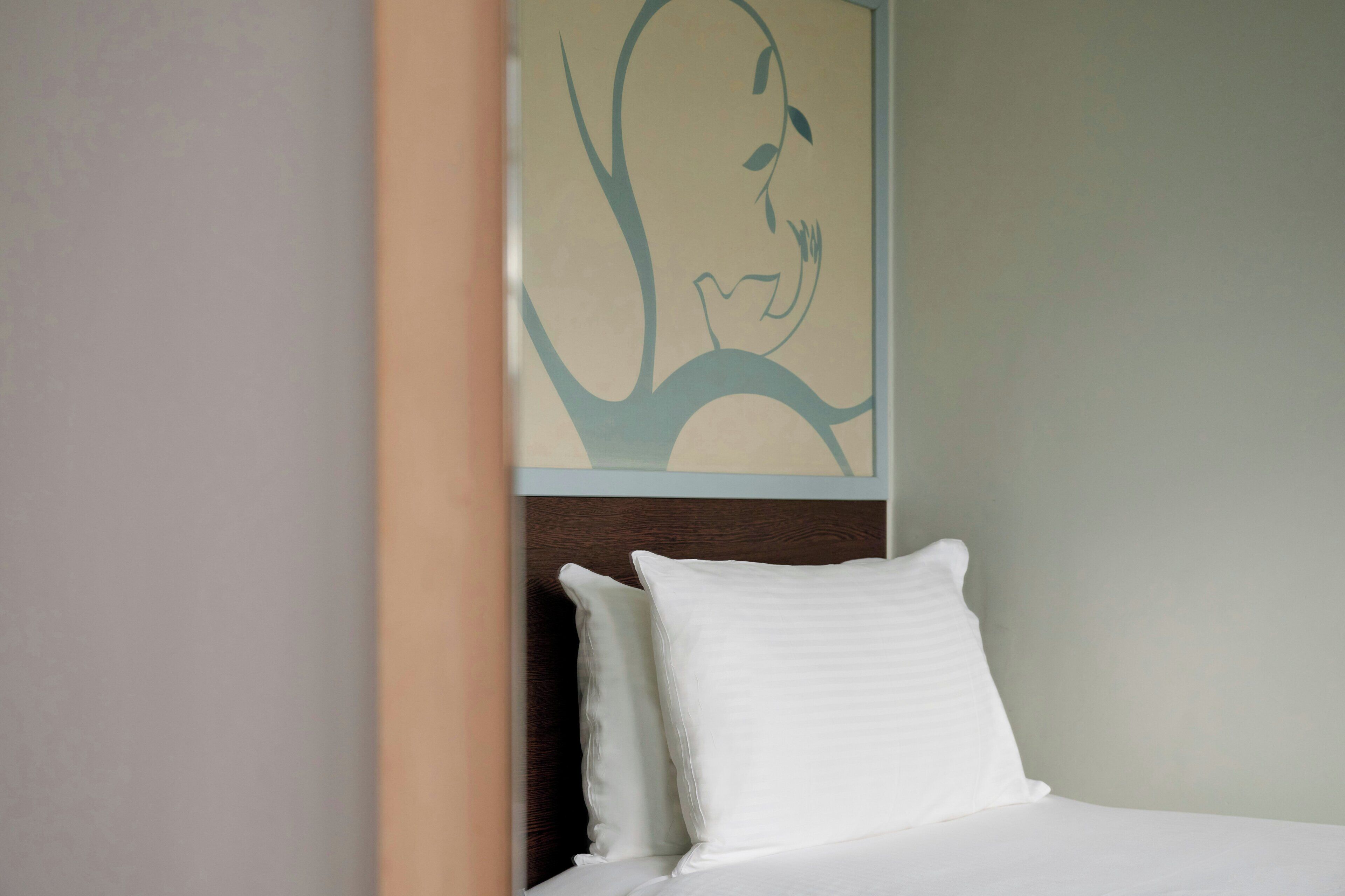 A bed with white bedding and pillows, a wooden headboard, and a wall with a framed artwork.