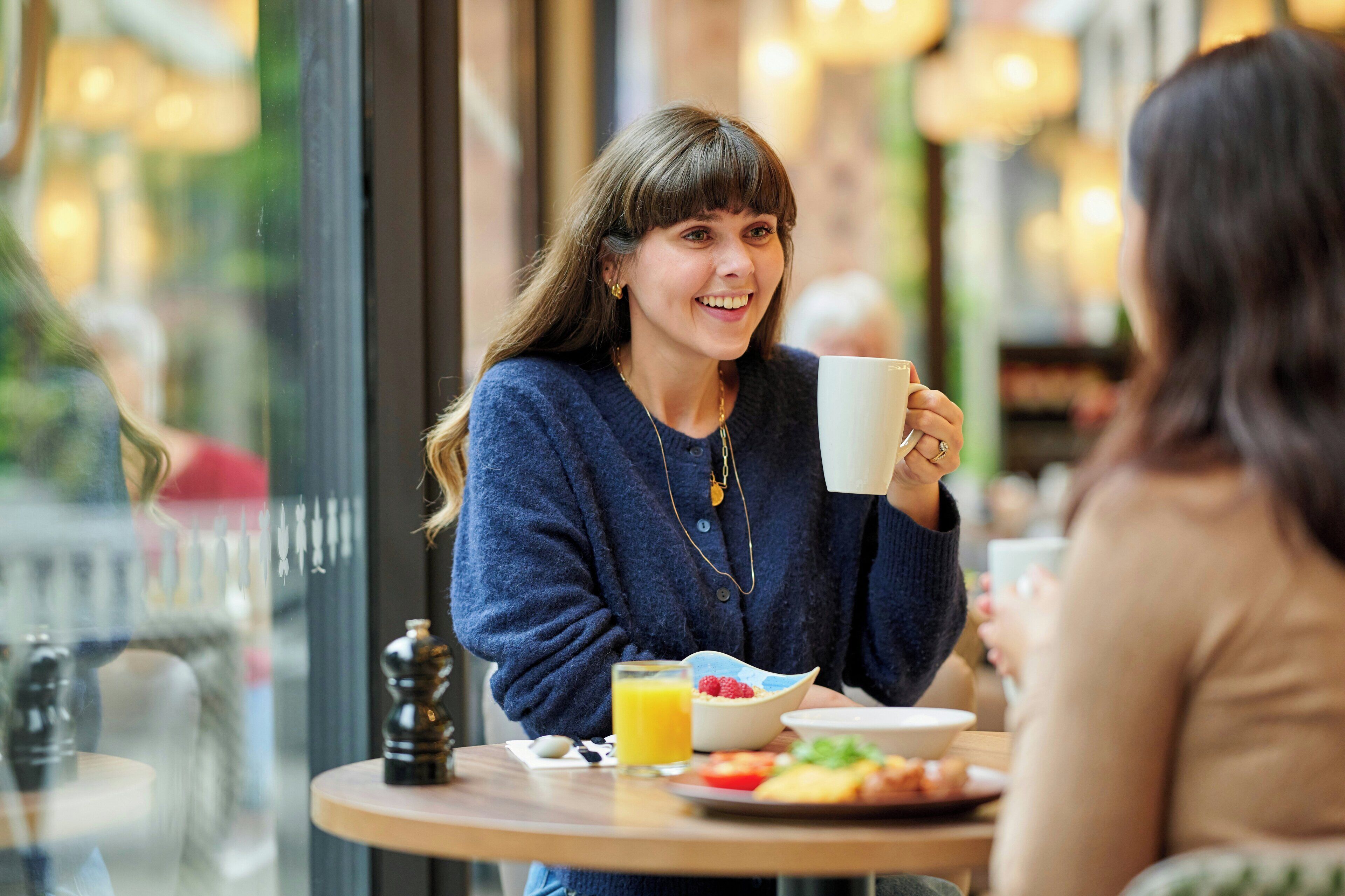 A person sitting at a table with a cup, a bowl of food, and a glass of orange juice.