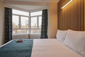 A hotel room with a large window, a bed with white linens, and a view of buildings outside.