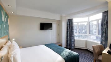 Habitación de hotel con una cama grande, un escritorio, una silla, un televisor y una ventana con vistas a la ciudad.