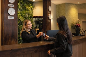 A reception desk with clocks labeled 'LONDON' and 'PARIS,' and a person handing over a card. - Bedford Hotel (London)