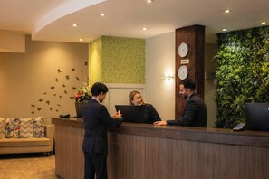A reception desk with a clock, a plant wall, and a sofa with patterned cushions.