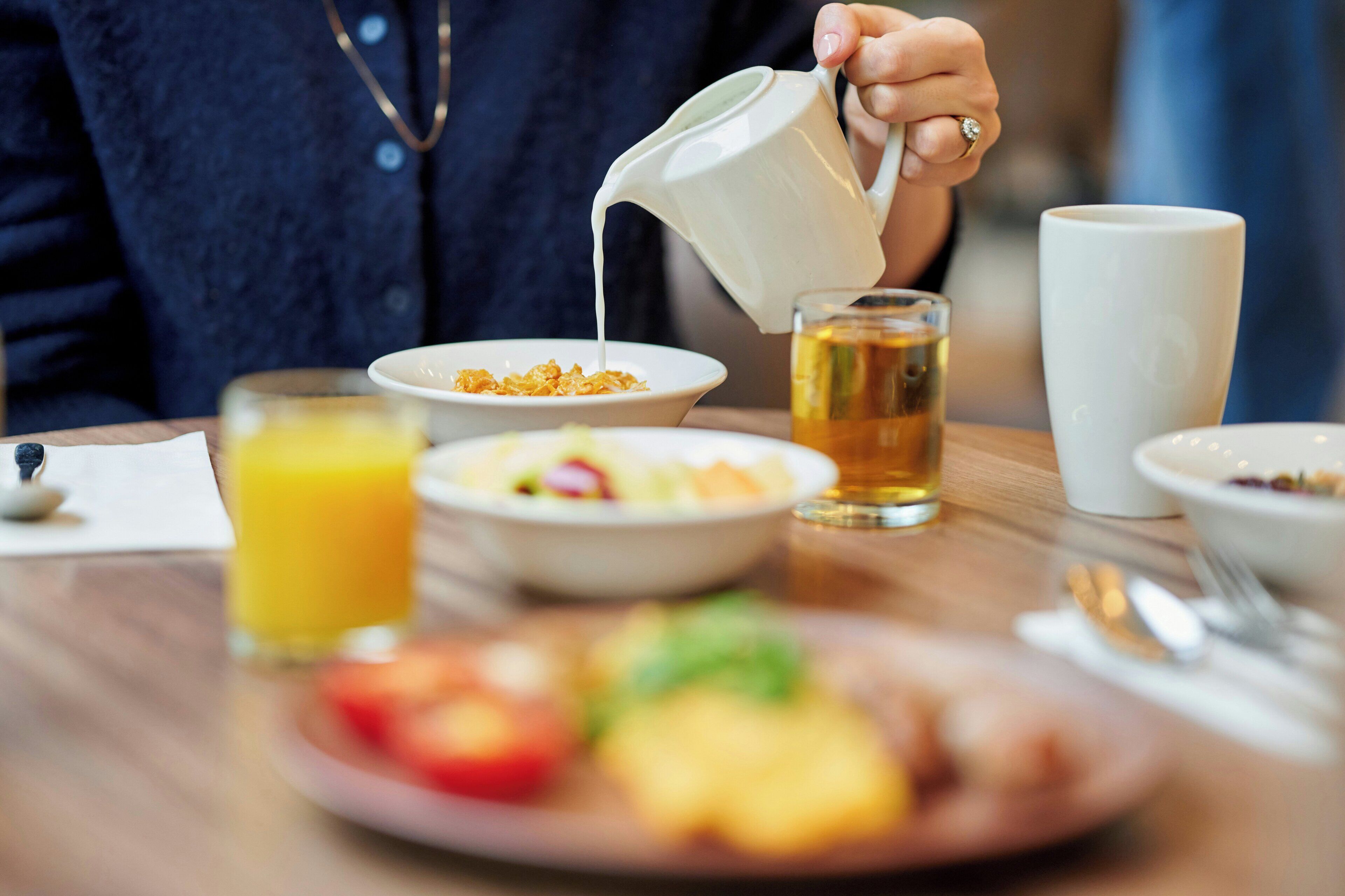 A breakfast setting with a person pouring a beverage into a cup, a glass of orange juice, and various dishes on the table.