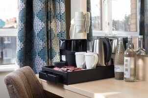 A hotel room with a coffee station, including a coffee maker, mugs, and a tray of snacks.
