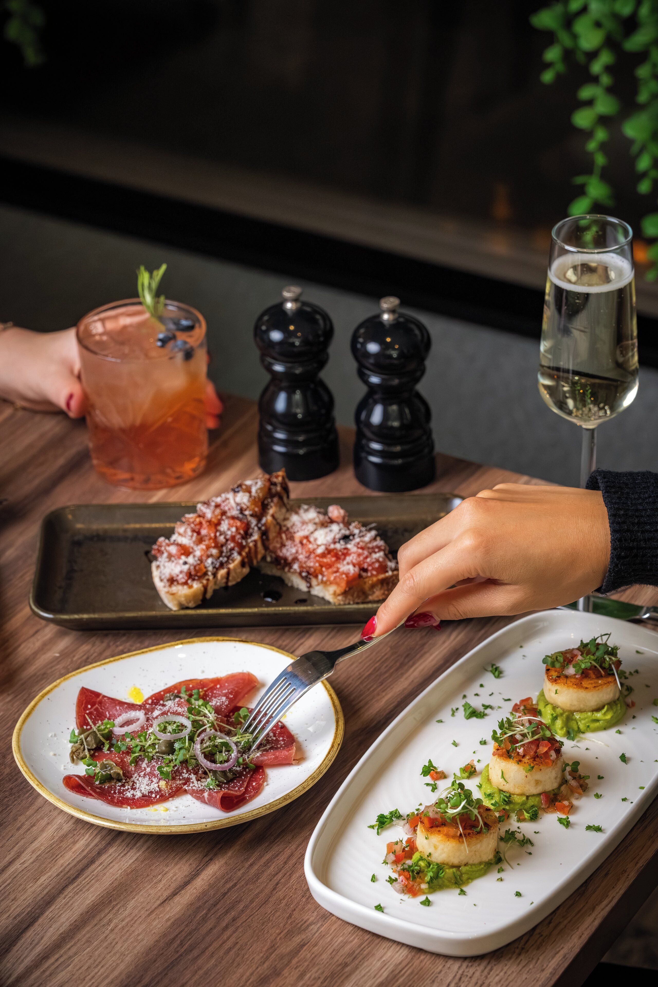 A dining table with a variety of dishes, including a plate of raw meat, a glass of iced tea, and a glass of white wine.
