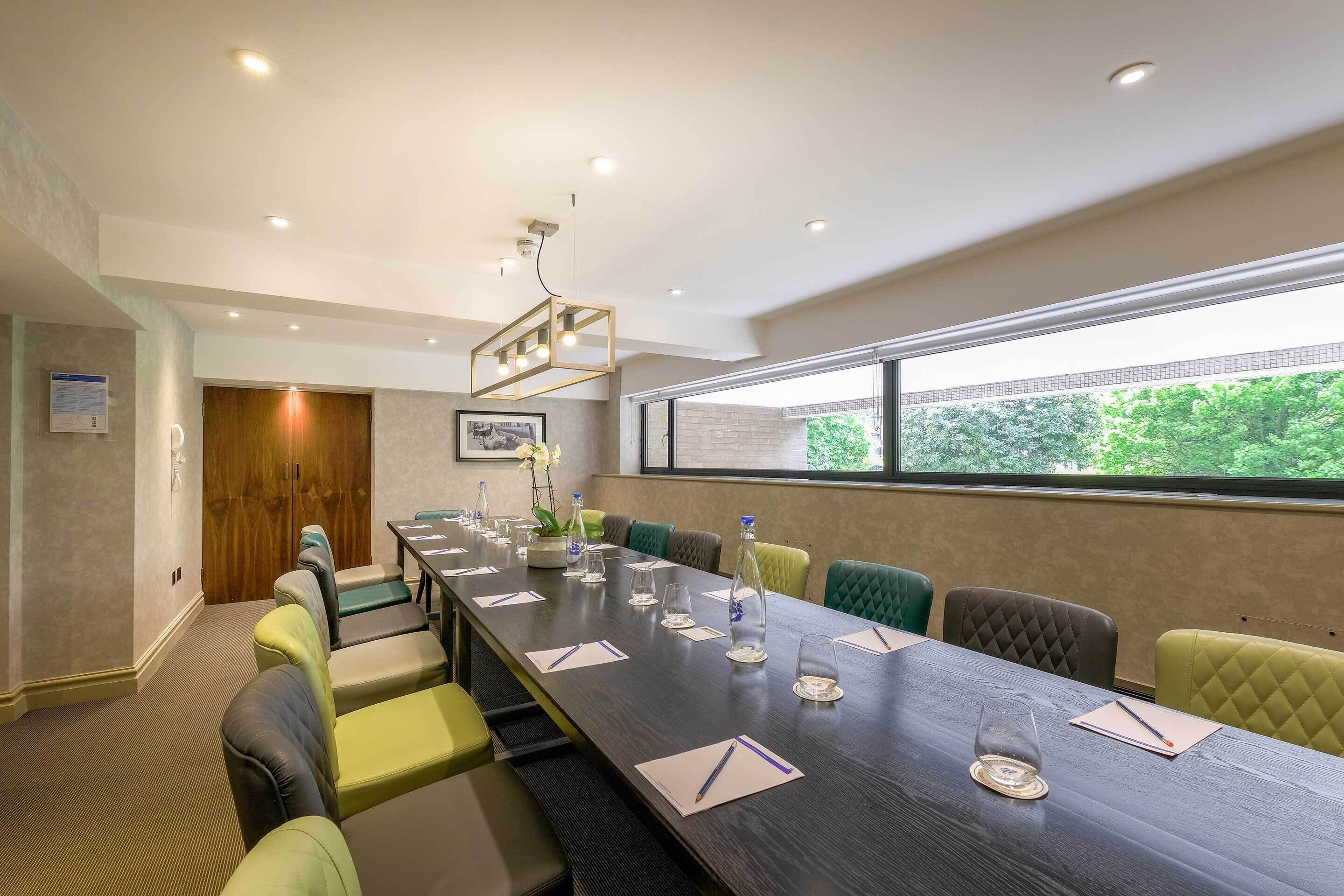 A conference room with a long table, multiple chairs, and a large window with a view of trees.