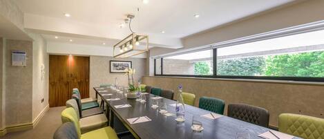 A conference room with a long table, multiple chairs, and a large window with a view of trees.