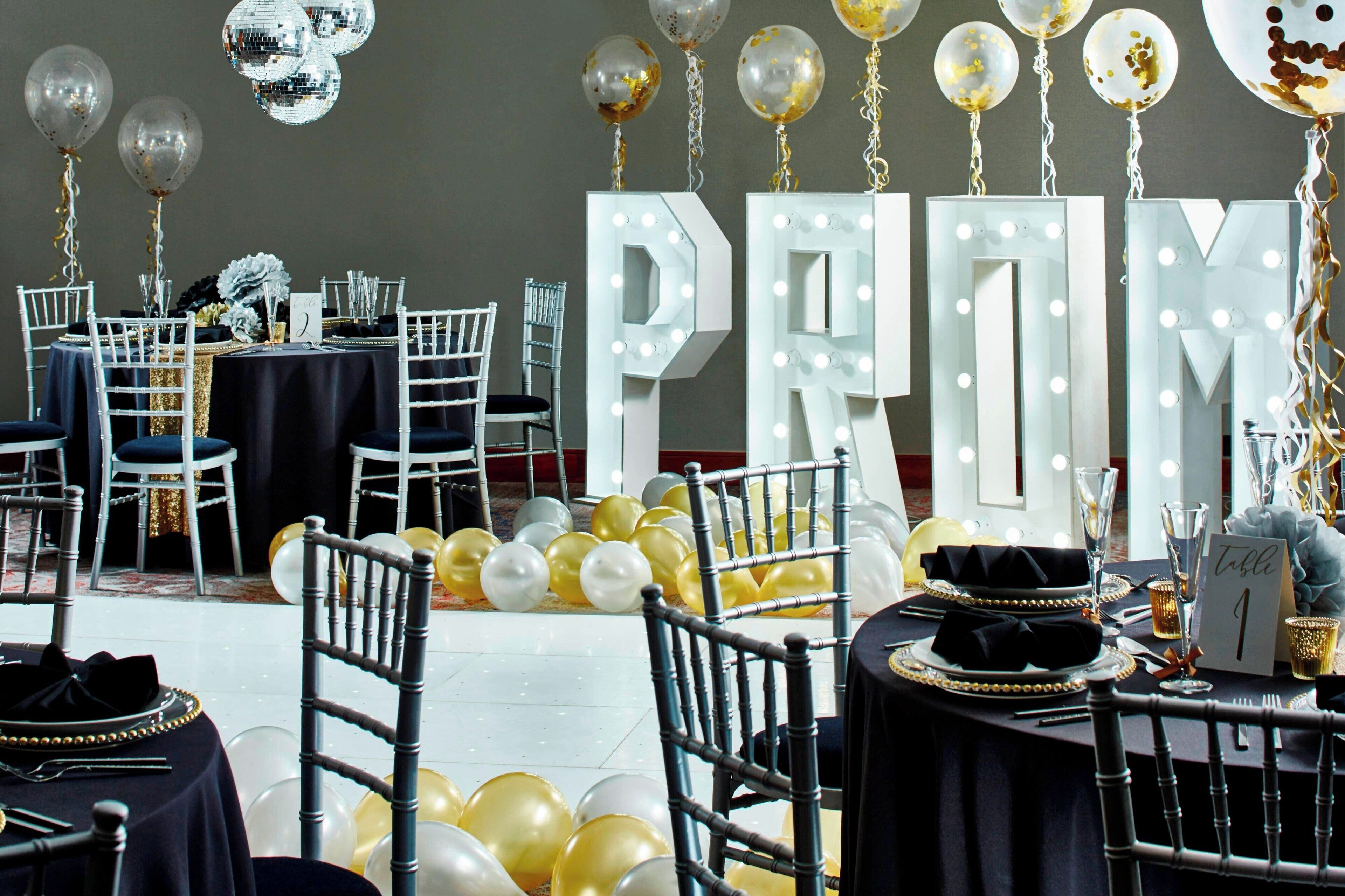 A formal dining area with tables set for a special event, featuring illuminated letters and balloons.