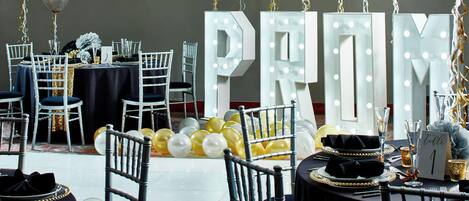 Un comedor elegante con mesas dispuestas para un evento especial, con letras iluminadas y globos.