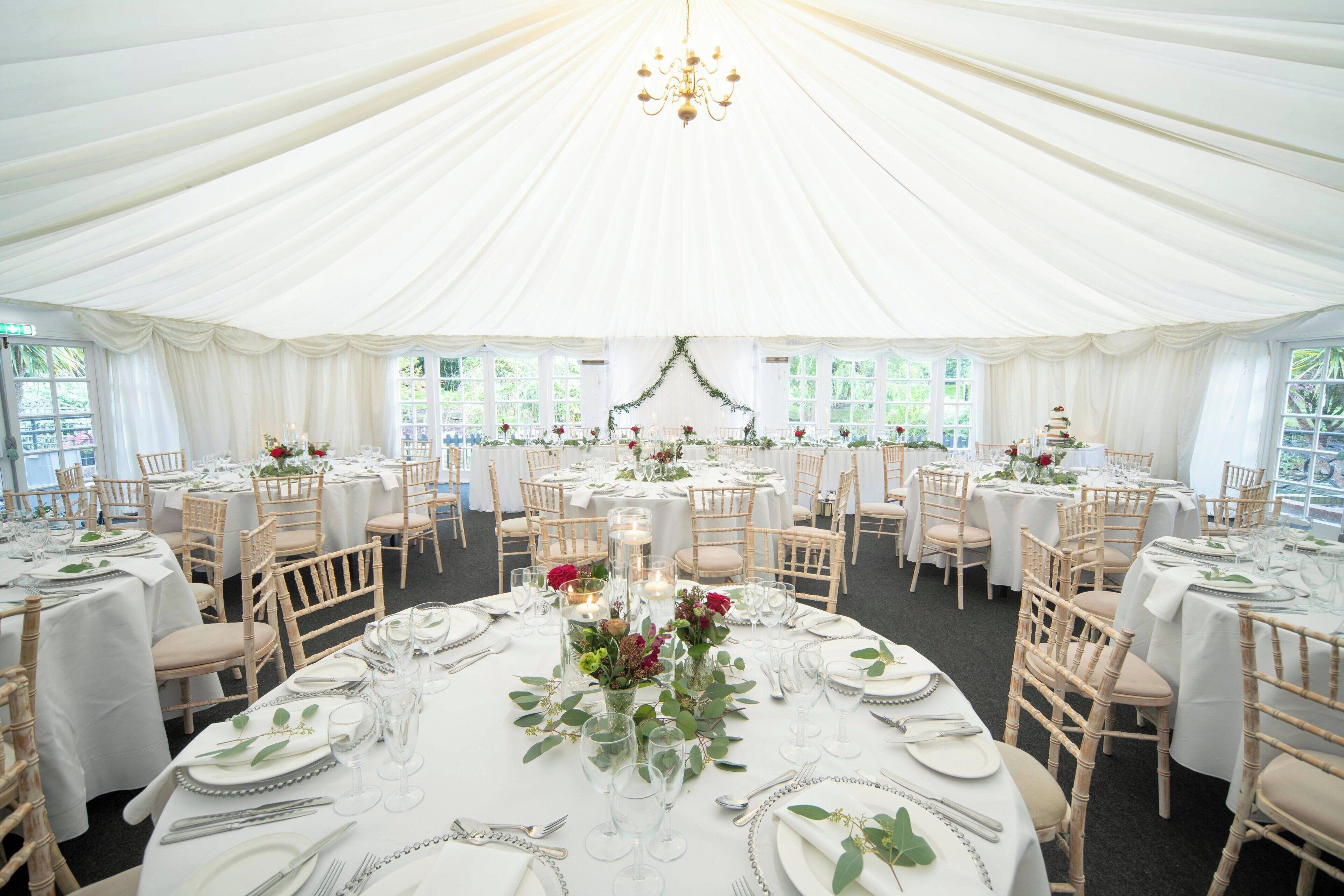 Un espacio para eventos con carpas, mesas redondas, manteles blancos y centros de mesa florales.
