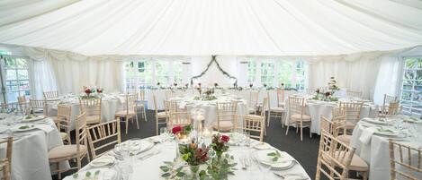 Un espacio para eventos con carpas, mesas redondas, manteles blancos y centros de mesa florales.