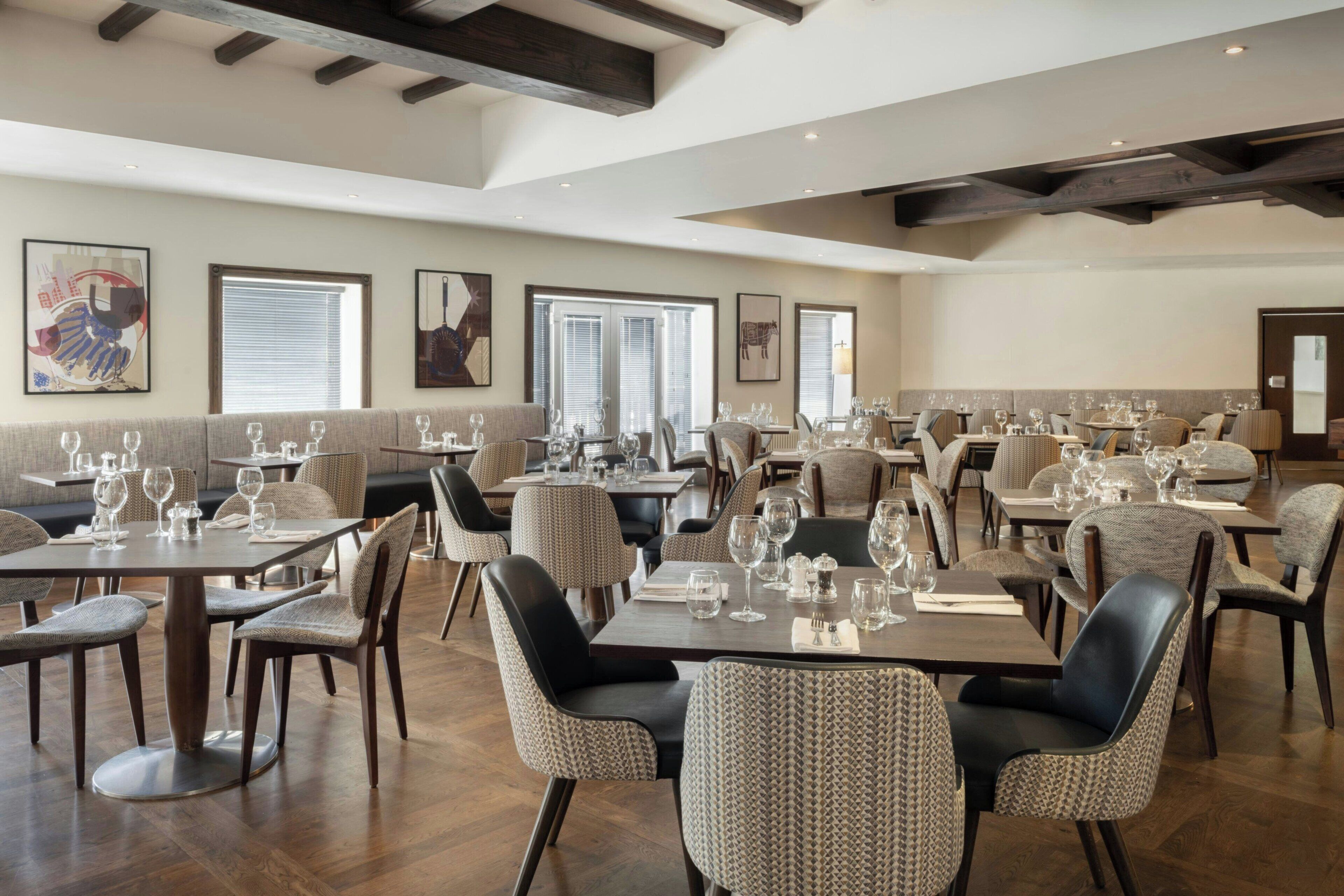 A restaurant with multiple dining tables and chairs, large windows, and artwork on the walls.